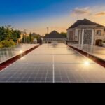 Solar panels covering a residential rooftop at sunset, reflecting light from the golden sky.] ,