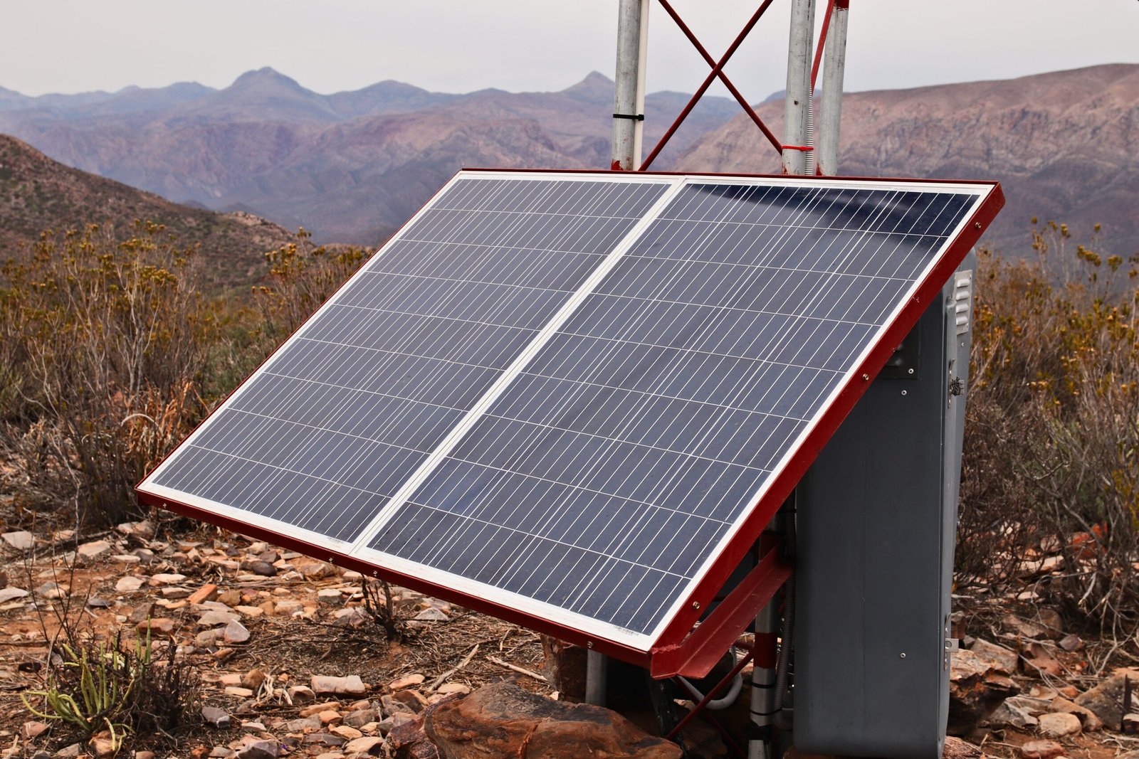 Solar panels mounted on a metal frame in a rocky desert landscape with distant mountains in the background, angled toward the sky.